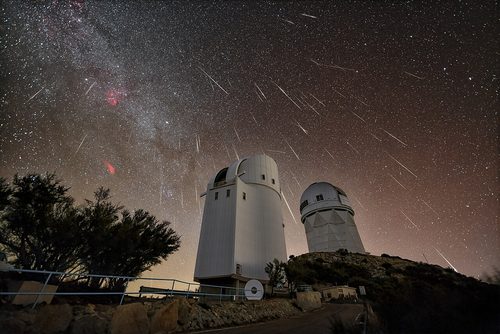 Geminid meteors streaking across a starry sky above white telescope domes at Kitt Peak